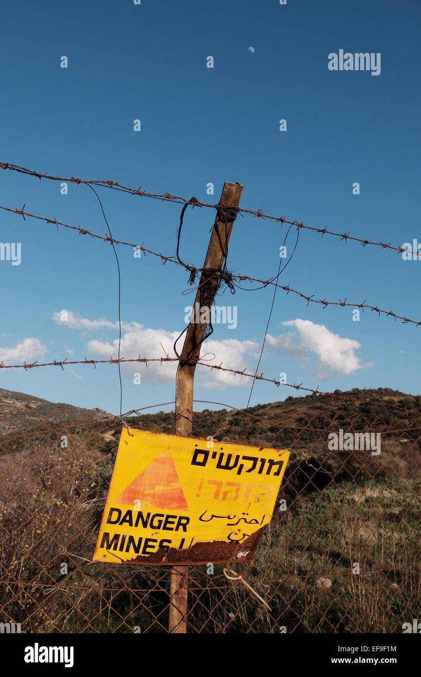 Israël. 29 janvier, 2015. Un panneau met en garde contre des mines de terre dans un champ adjacent à la frontière libanaise, le village de Ghajar Alaouites syriens (extrême gauche) et le poste de contrôle des FDI à laquelle une attaque de missiles du Hezbollah sur un convoi des FDI le 28 janvier 2015 a tué deux soldats et en ont blessé plusieurs autres (à droite). Israël maintient un haut niveau d'alerte tout en permettant aux résidants de la région de revenir aux affaires courantes. Credit : Alon Nir/Alamy Live News Banque D'Images