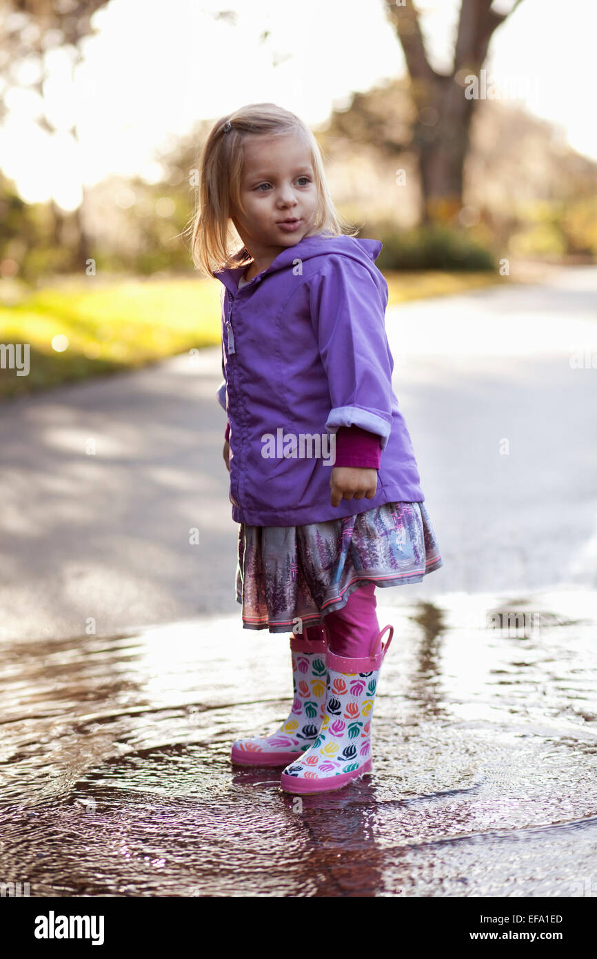 Une petite fille portant des bottes de pluie se trouve dans une flaque  d'eau dans la rue Photo Stock - Alamy