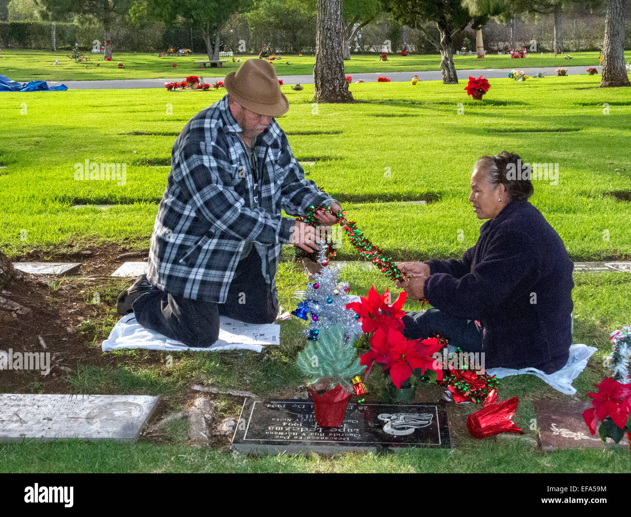 A Noël, un vieux couple décorer un membre de la pierre tombale dans un cimetière de l'Orange, CA. Banque D'Images