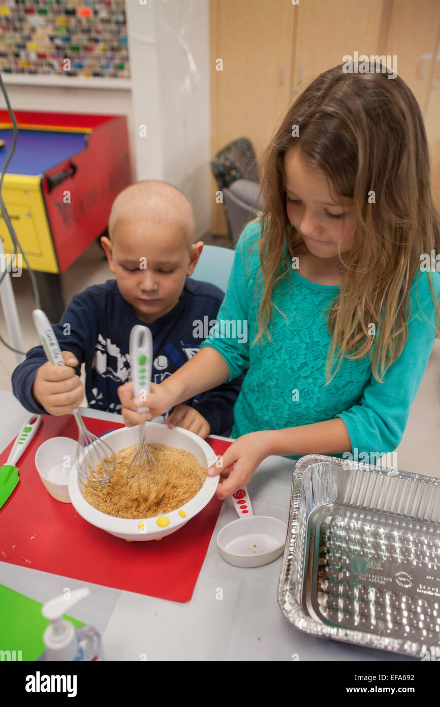 Les 8 ans de la sœur d'un patient de cancer chimiothérapie choc à l'Hôpital pour enfants de l'Orange, CA, aide son frère un faire un dessert de potiron. Le soutien familial est un important service de l'hôpital. Remarque tête chauve. Banque D'Images