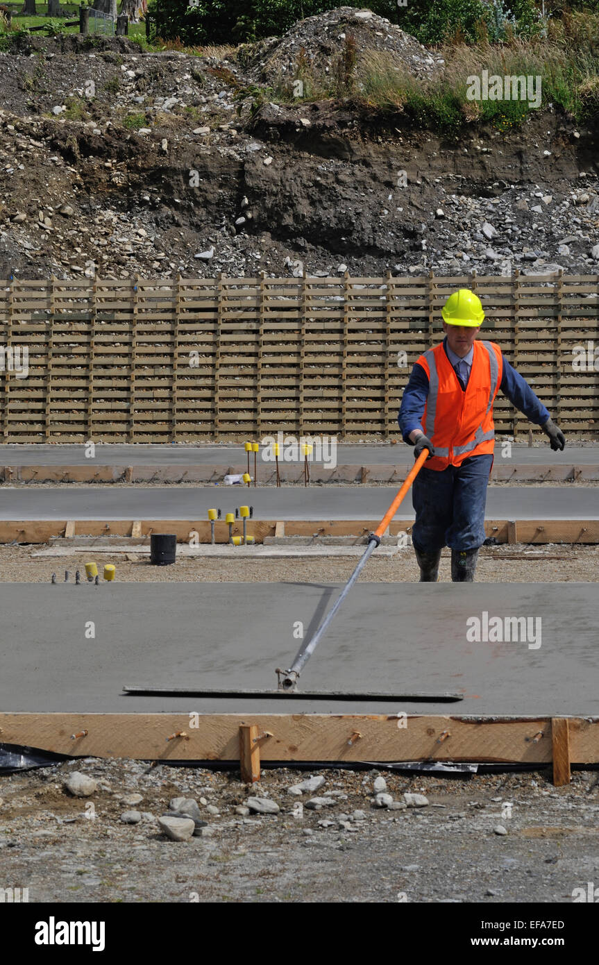 Un constructeur utilise une longue poignée d'une truelle pour flotter une dalle de béton humide pour un grand bâtiment Banque D'Images