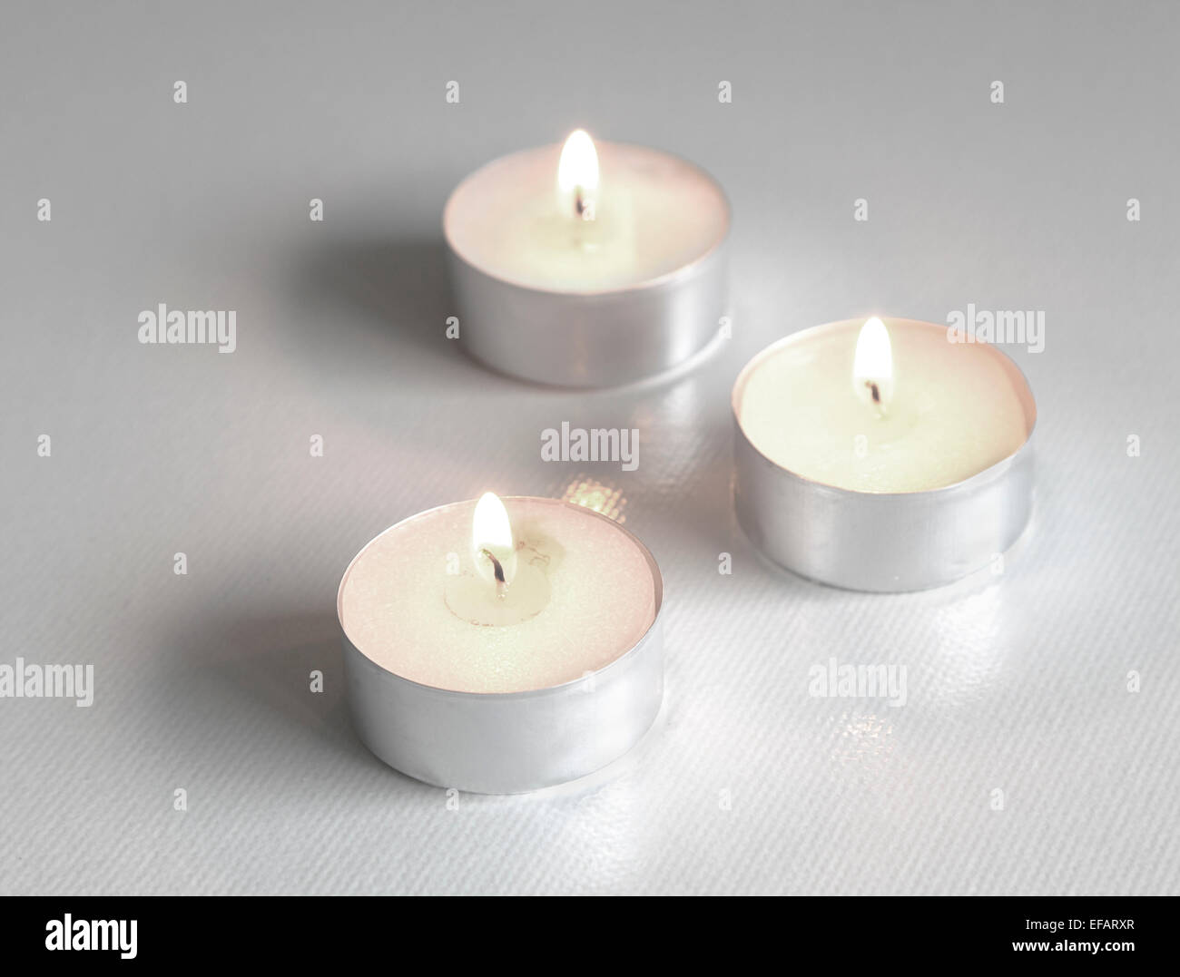 Trois blancs, allumé des bougies thé formant un triangle sur un fond blanc Banque D'Images