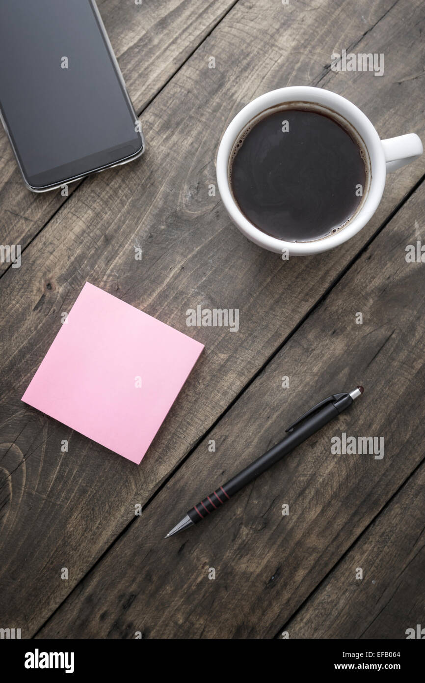 Smart phone avec sticky note papier et tasse de café sur le vieux bureau en bois. Banque D'Images