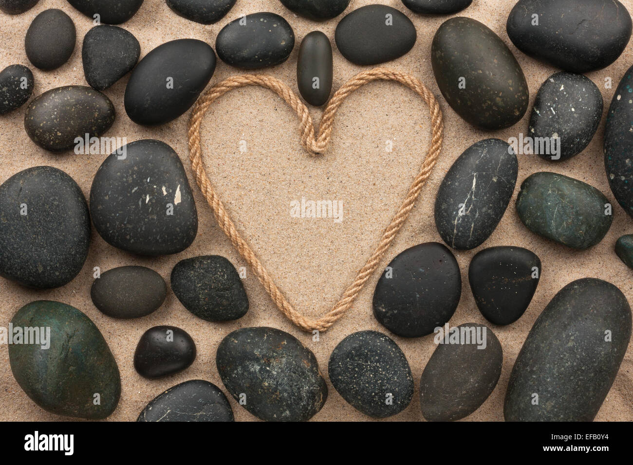 Beau cadre de corde dans la forme de coeur avec les pierres noires, sur le sable Banque D'Images