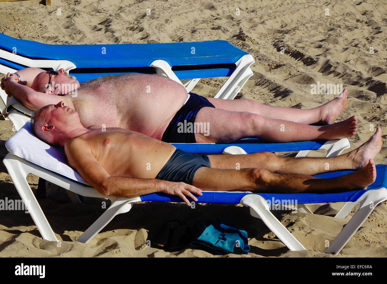 Deux hommes d'âge moyen de bronzer sur les transats avec des agrégations sur, Benidorm, Costa Blanca, Espagne Banque D'Images