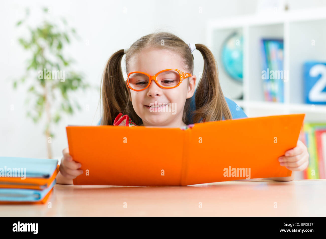 Happy funny girl enfant dans les verres de la lecture d'un livre à l'école primaire Banque D'Images
