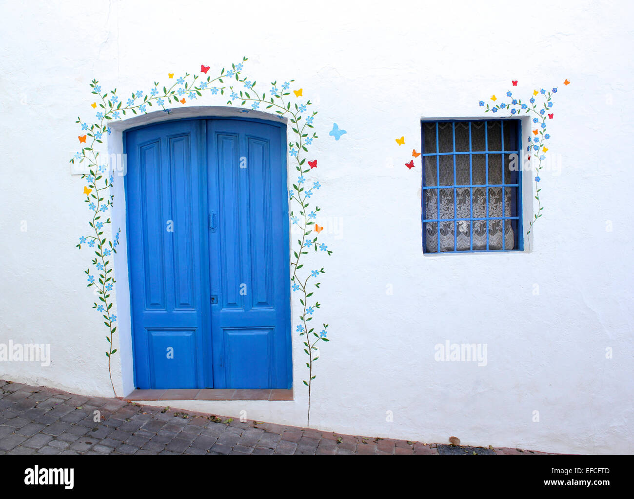 Une porte bleu peint de couleurs vives et fenêtre décorée de la murale d'un trailing plantes et fleurs sur un mur blanchi à la chaux Banque D'Images