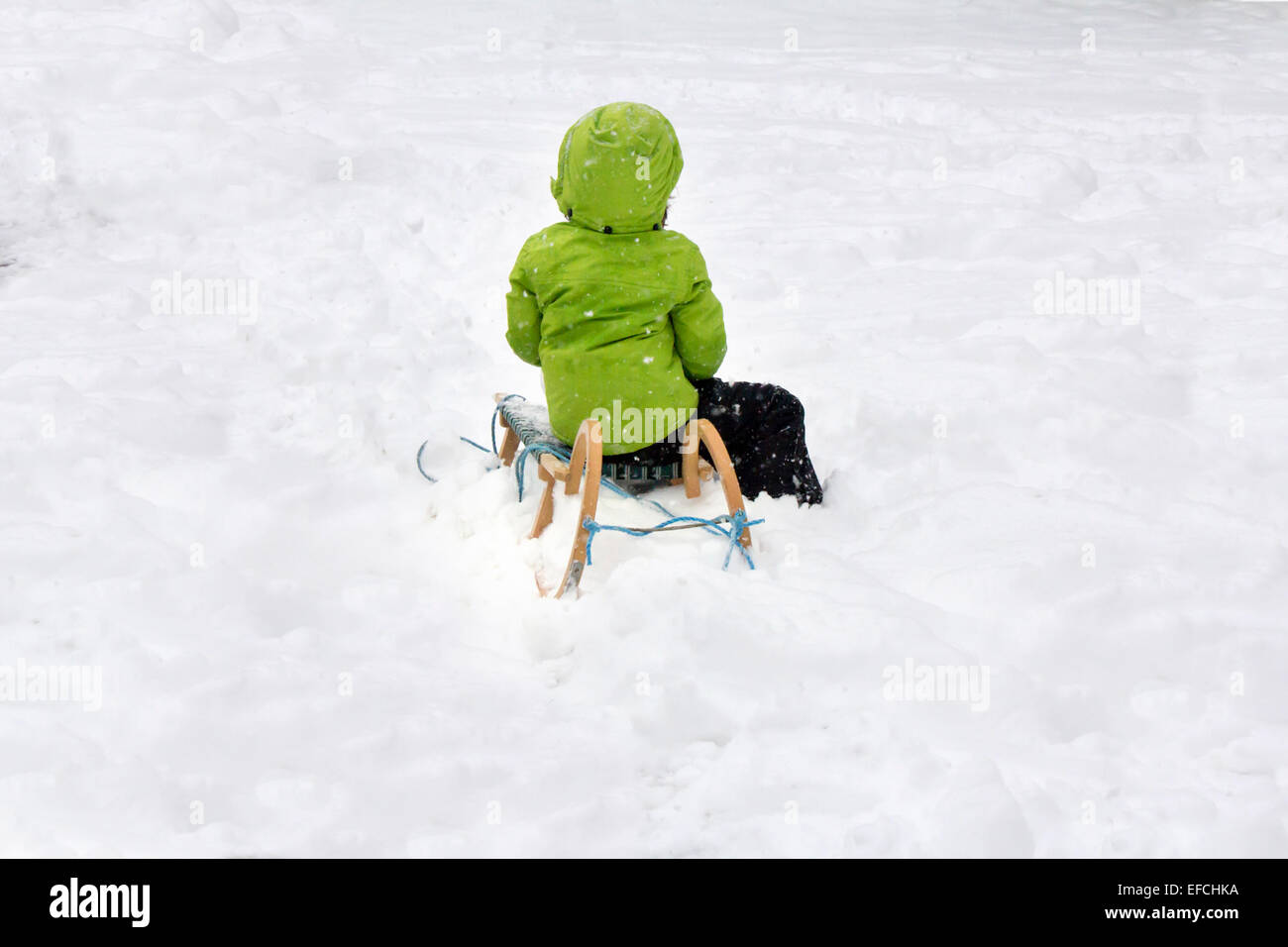 Enfant dans une gaine verte bénéficiant d'une promenade en traîneau dans la neige winter park Banque D'Images