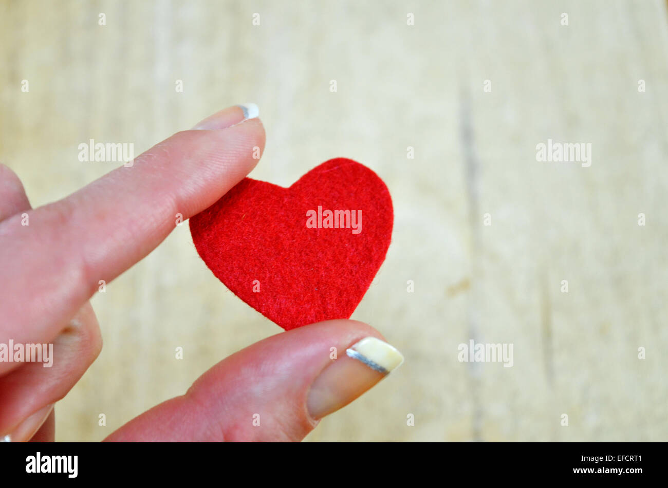Petit coeur rouge tenue par les doigts sur un fond de bois Banque D'Images
