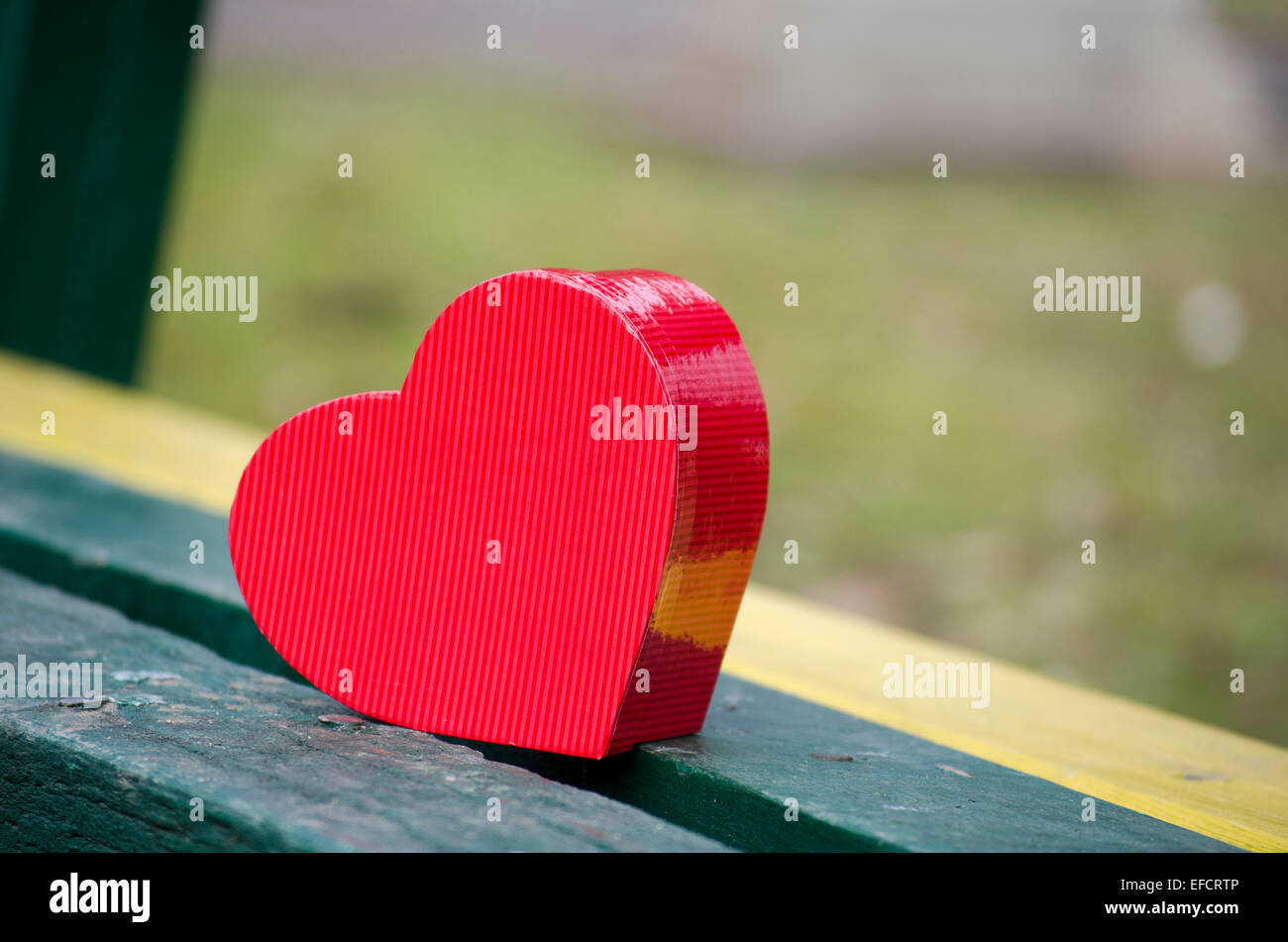 Red Heart shaped box sur un banc de parc en bois tourné à l'extérieur, Banque D'Images