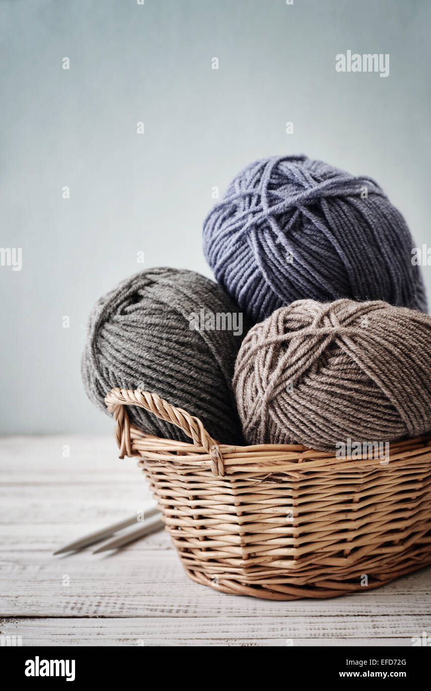 Fil de laine en rouleaux avec des aiguilles à tricoter dans le panier en osier sur fond bleu clair Banque D'Images