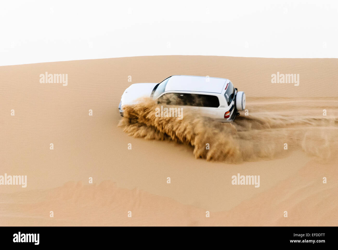 Un 4x4 hors route jeep lance de sable comme il se conduit sur le côté d'une dune de sable dans le désert de la péninsule arabique Banque D'Images