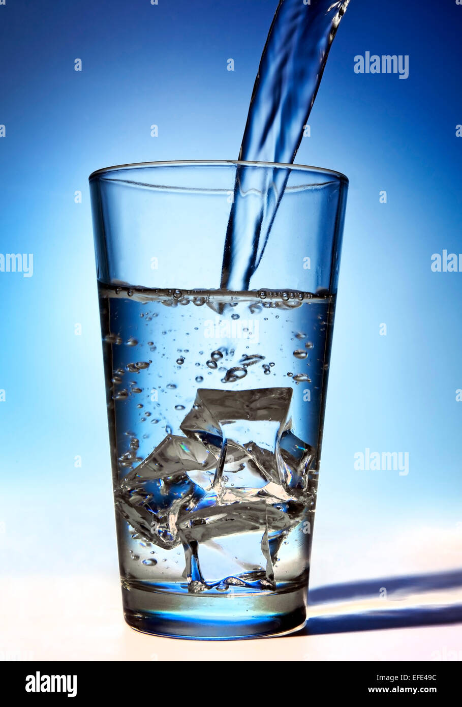 L'eau est versé dans un verre avec des glaçons. Banque D'Images