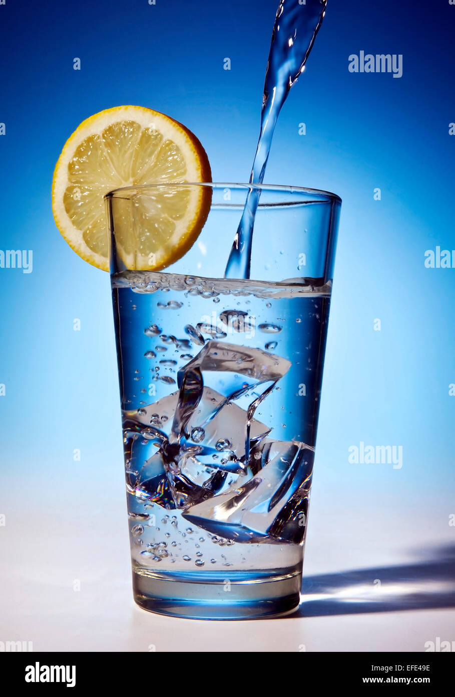 L'eau est versé dans un verre avec des glaçons et une tranche de citron Banque D'Images