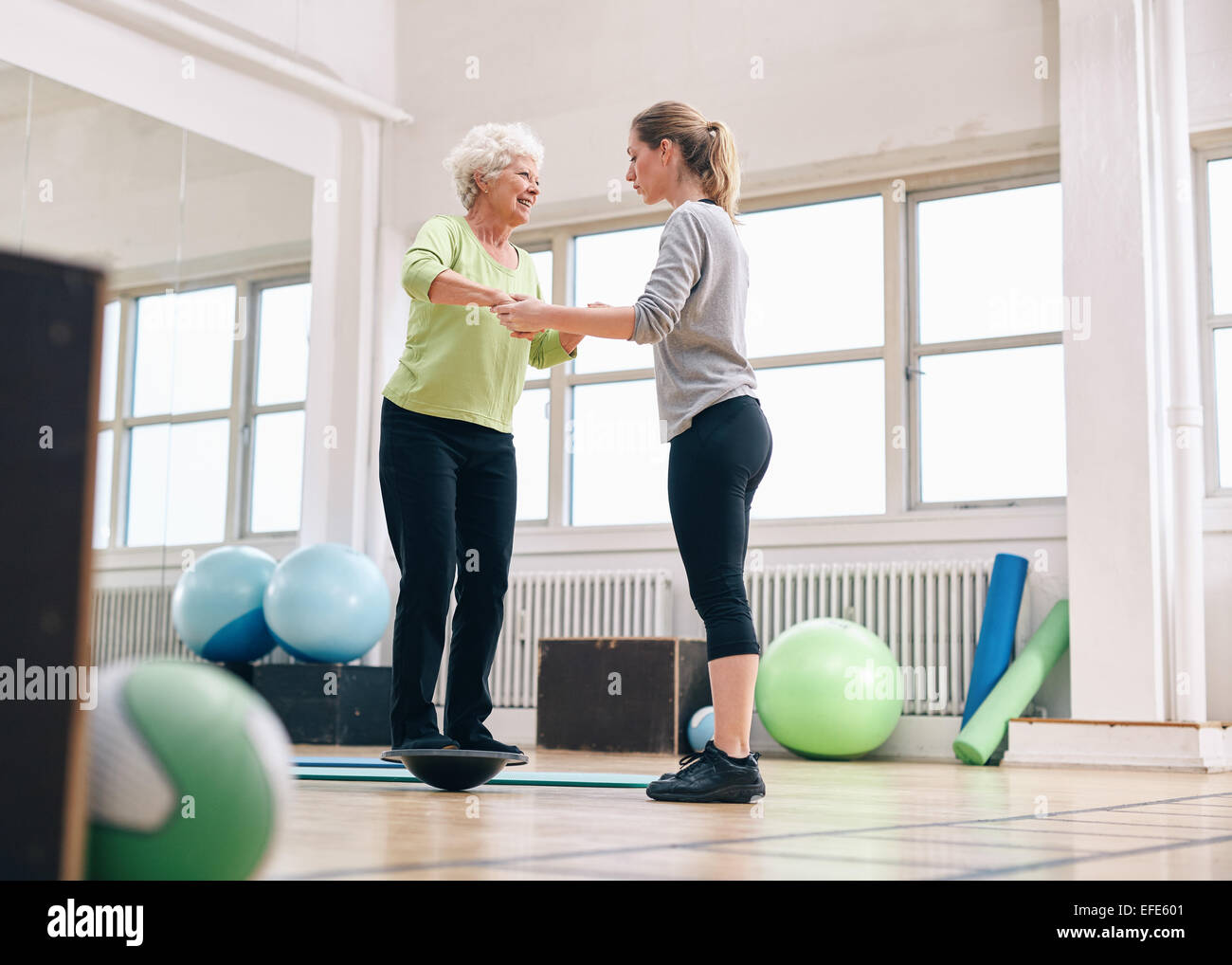 Femme trainer helping senior woman in a gym entraînement avec le bosu balance plate-forme de formation. La femme d'être assisté d'une salle de sport Banque D'Images