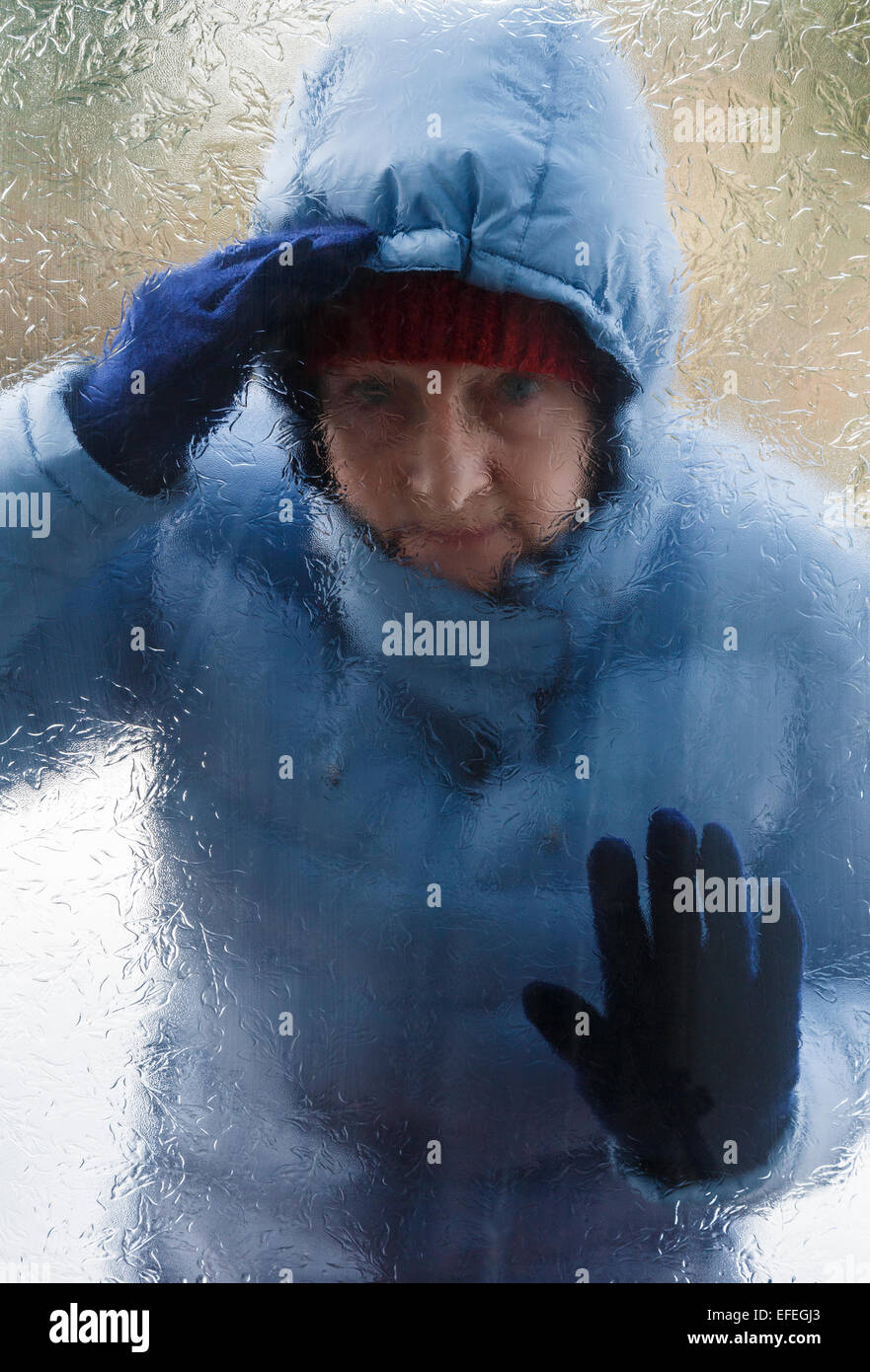 Une femme portant un épais manteau chaud à l'extérieur en regardant par la fenêtre d'une porte en verre dépoli qui veulent venir dans à froid. Angleterre Royaume-uni Grande-Bretagne Banque D'Images