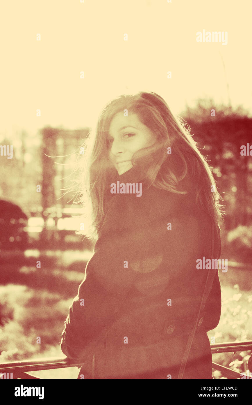 Une jeune fille aux longs cheveux bruns à la recherche Retour à l'appareil photo avec sun flare pendant l'hiver Banque D'Images