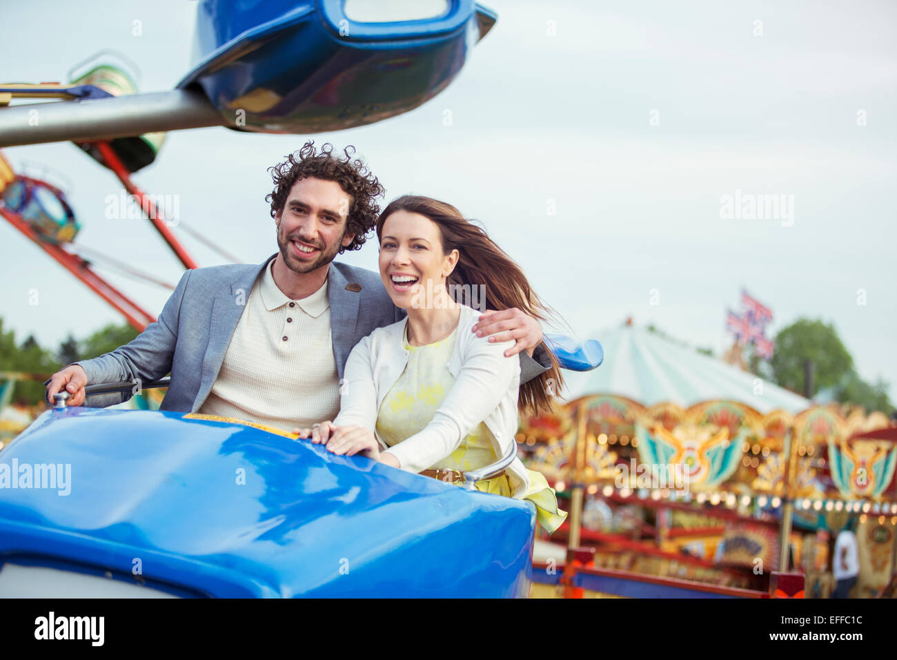 Couple enjoying ride sur carrousel en amusement park Banque D'Images