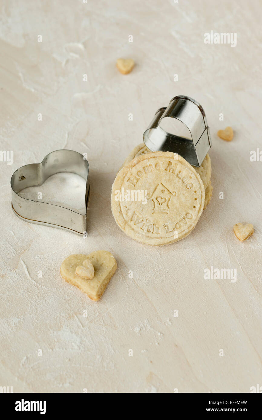 Les cookies faits maison et deux en métal en forme de cœur sur un emporte-pièce en bois Banque D'Images