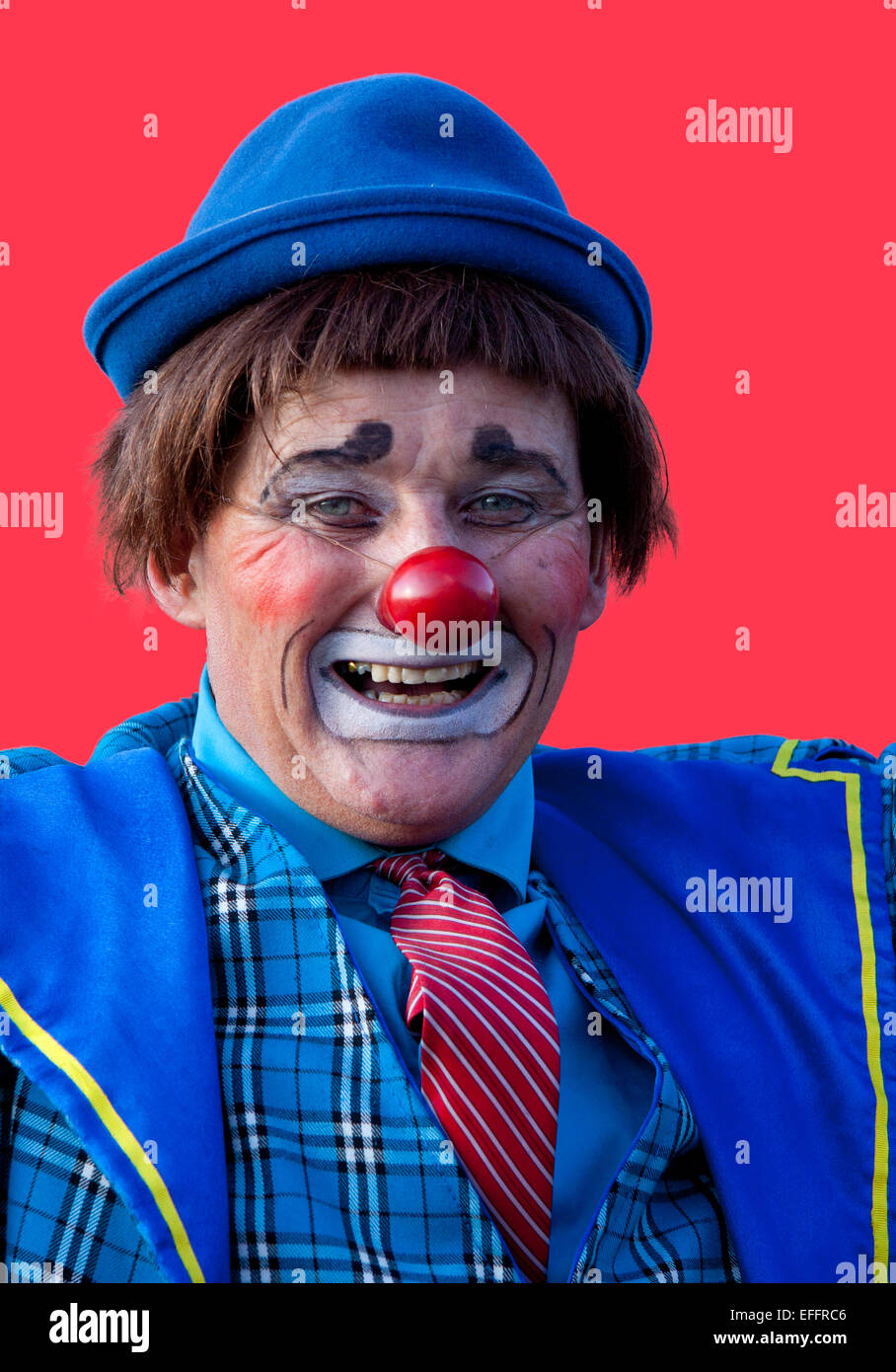 Clown de cirque en costume traditionnel avec un nez rouge isolé sur fond rouge. Banque D'Images