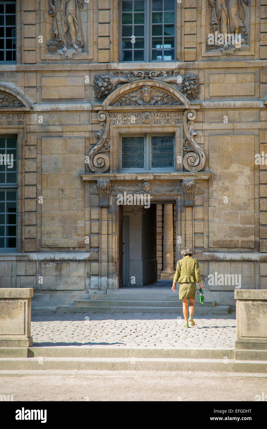 Woman walking through cour vers la porte de l'Hôtel de Sully, le Marais, Paris, France Banque D'Images
