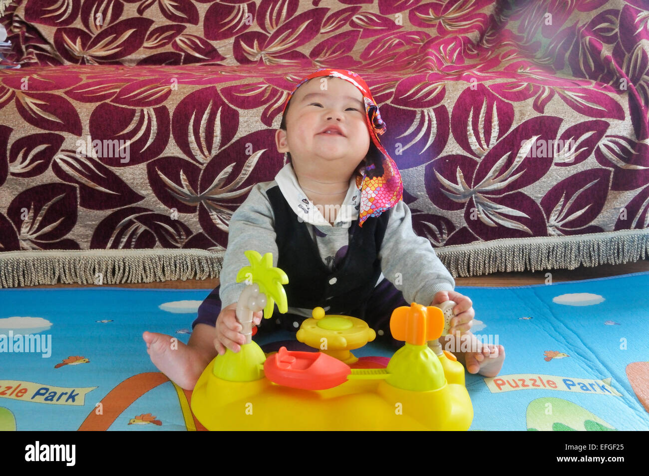 Mignon Bébé Garçon chinois avec foulard sitting on floor and playing with toy. Banque D'Images