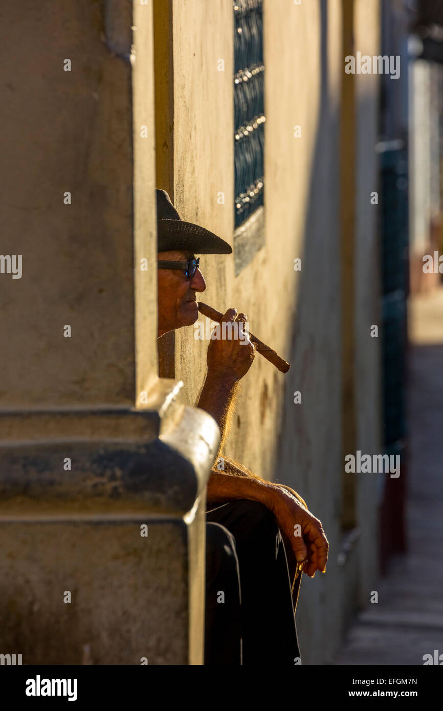 Un vieillard assis sur un Cubain porte dans la lumière du soir, fumer un cigare, Trinidad, la province de Sancti Spiritus, Cuba Banque D'Images