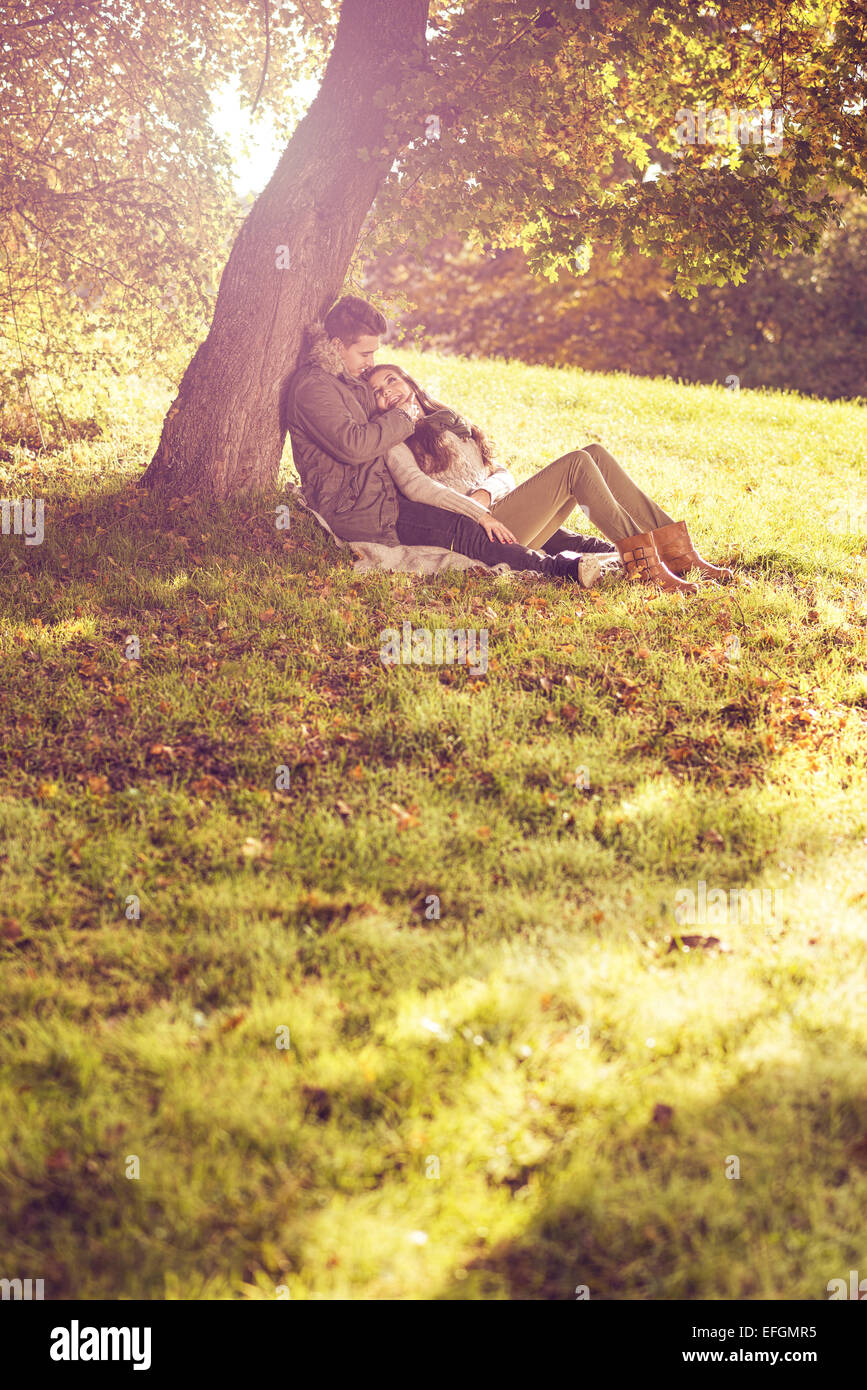 Love couple assis sous un arbre dans la forêt d'automne Banque D'Images