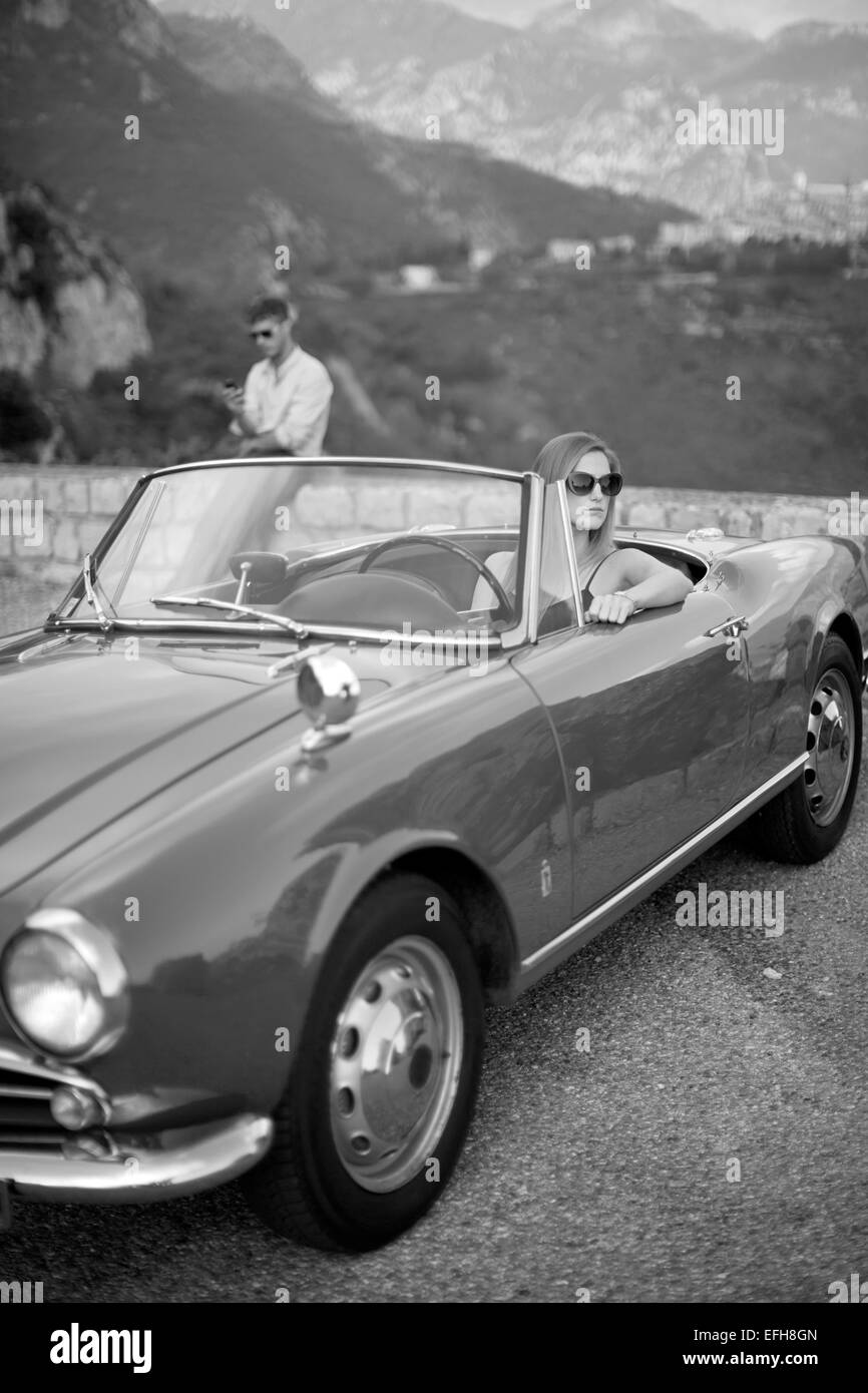 Jeune femme assise dans une voiture de sport vintage avec son petit ami dans l'arrière-plan Banque D'Images