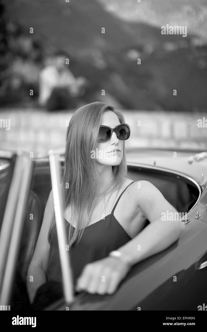 Jeune femme assise dans une voiture de sport vintage avec son petit ami dans l'arrière-plan Banque D'Images