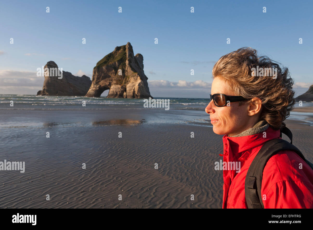 Femme sur la plage par un jour de vent, Archway îles dans l'arrière-plan, Wharariki Beach, South Island, New Zealand Banque D'Images