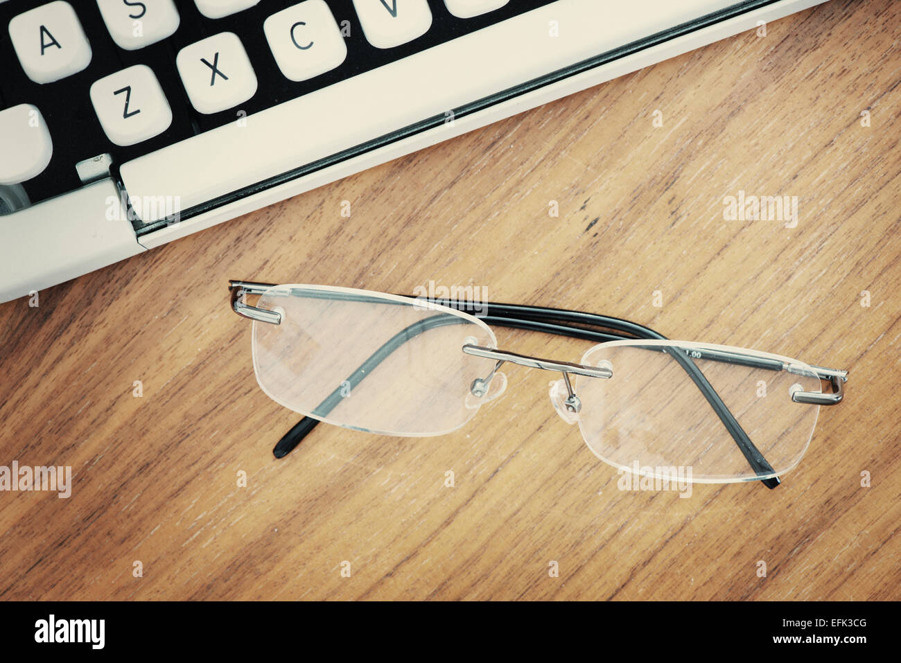 Vue du dessus de la machine à écrire à l'ancienne des années 70 et lunettes modernes sur table en bois. Banque D'Images