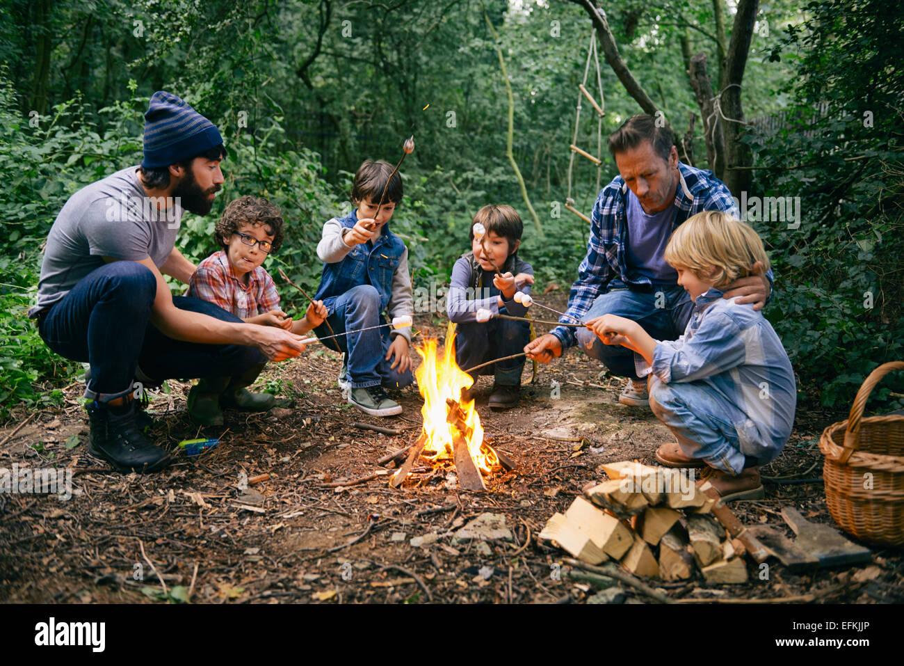Deux pères et quatre garçons toasting guimauves sur feu de forêt dans Banque D'Images