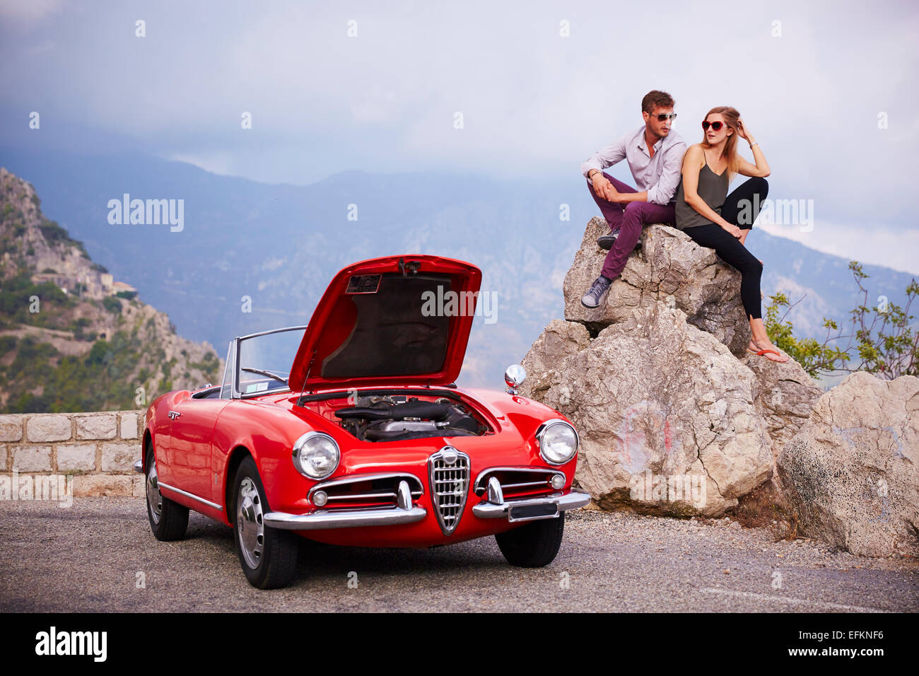 Couple assis en attente de secours avec une voiture classique réparties dans les montagnes françaises Banque D'Images