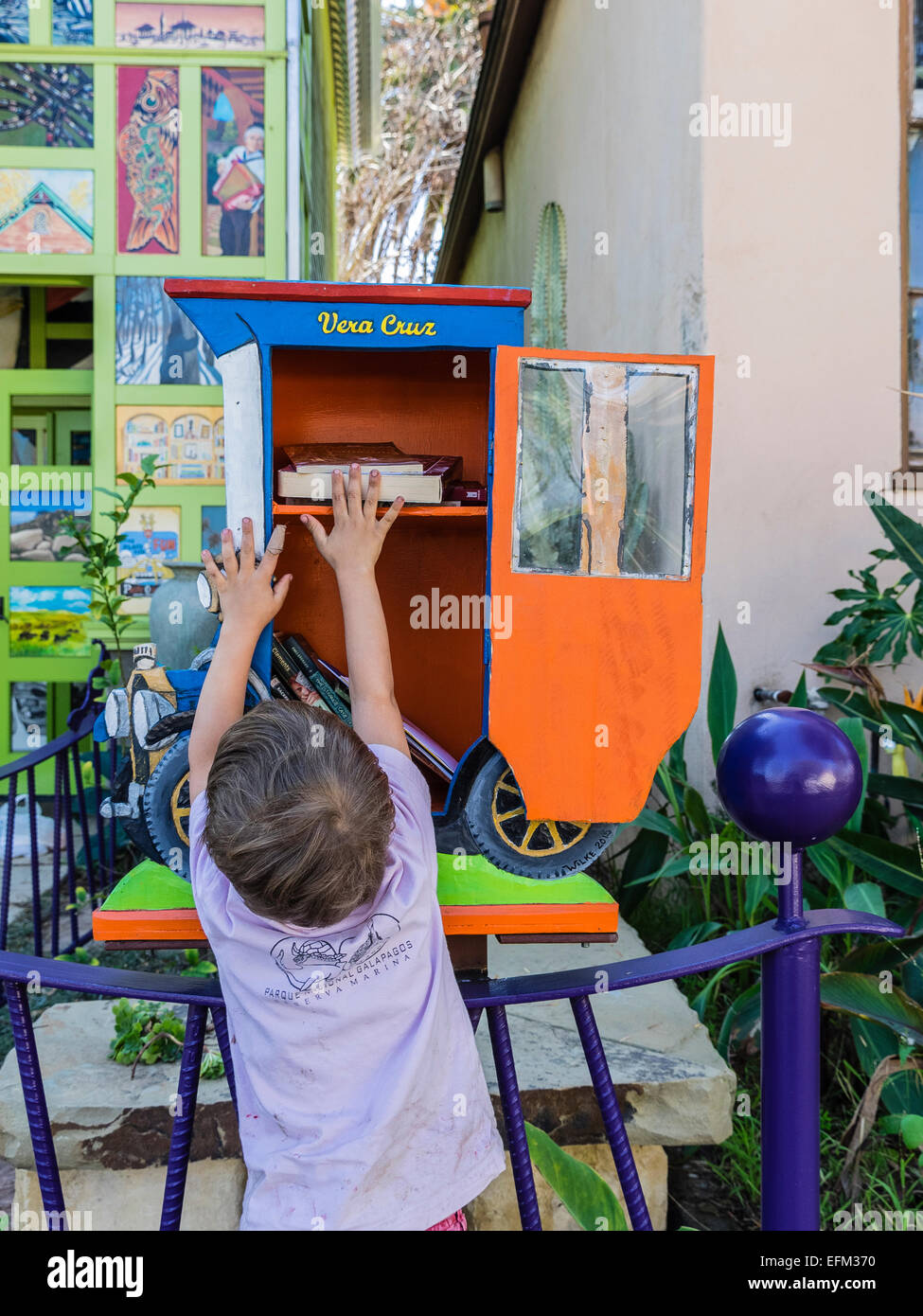 Un jeune garçon tient un livre qu'il vient d'une petite bibliothèque gratuite construit sous la forme d'une ancienne voiture. Banque D'Images