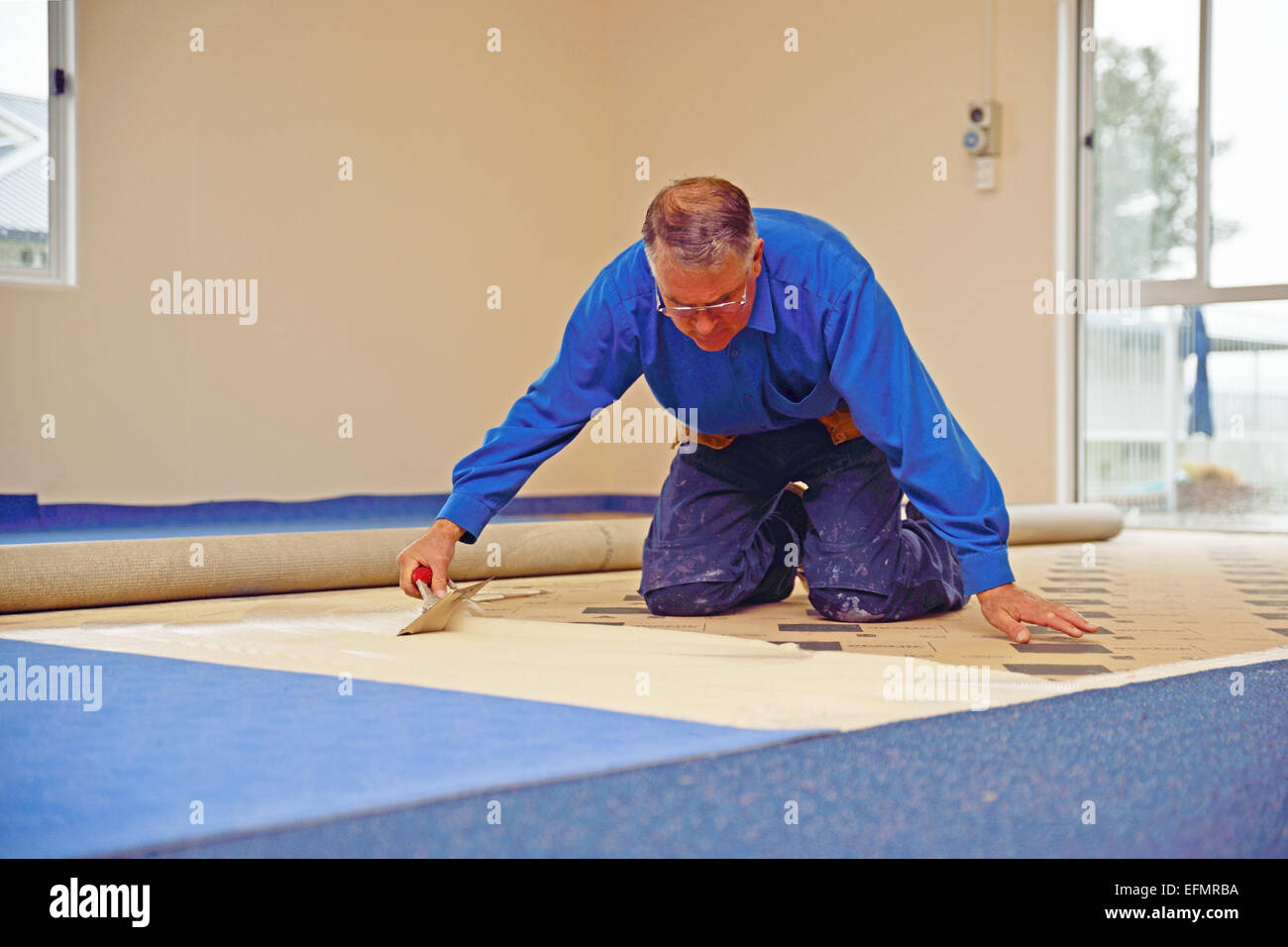 Un floorlayer s'étend sur la sous-couche adhésive pour un travail de pose de tapis Banque D'Images