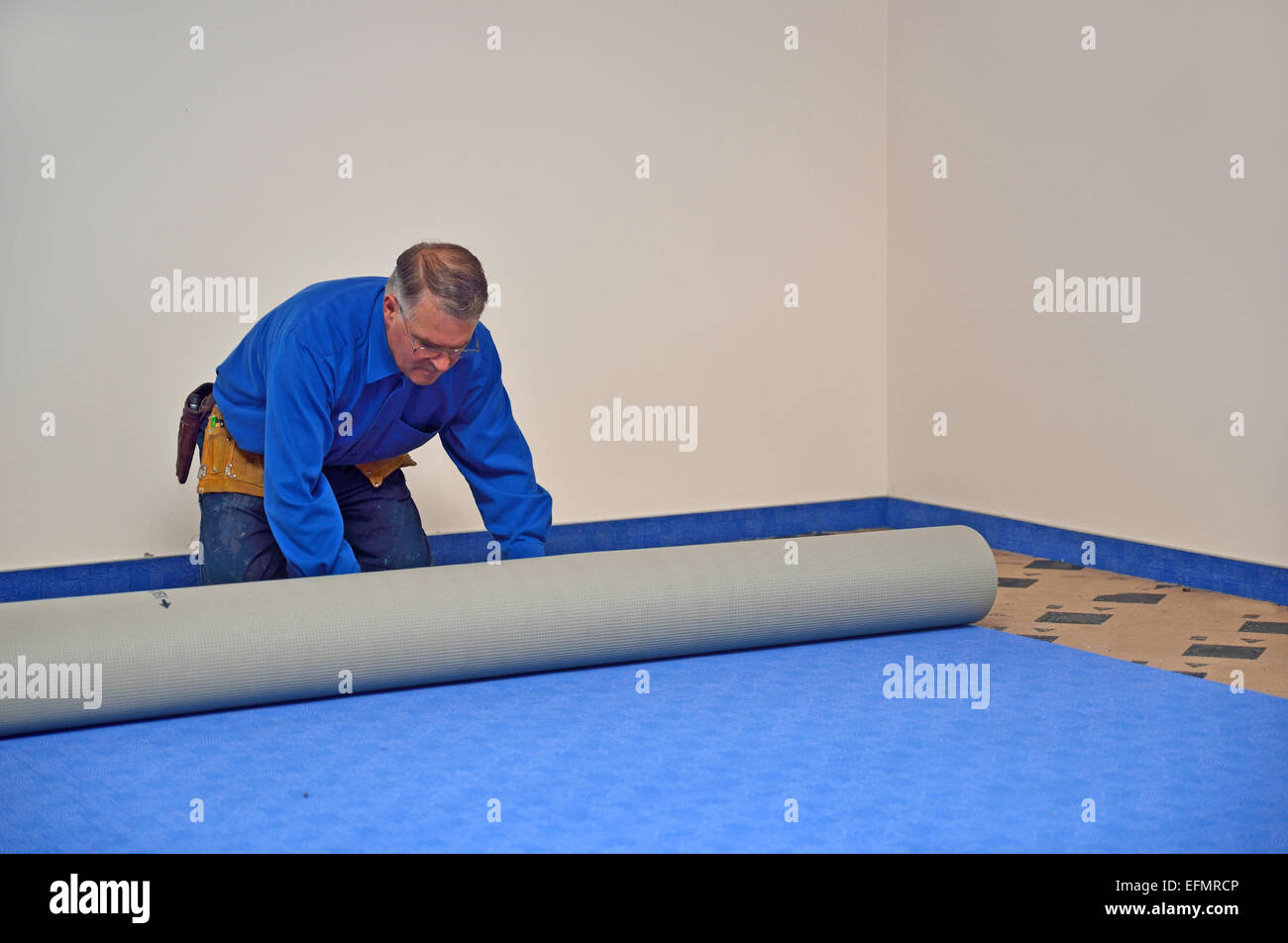 Un floorlayer déroule le tapis dans un nouveau travail d'floorlaying Banque D'Images