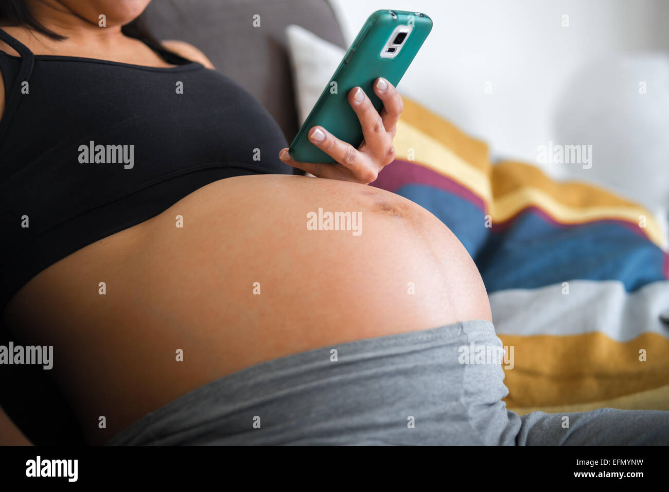 Baby bump, Image d'une femme enceinte de 8 mois maintenant un téléphone mobile. Banque D'Images