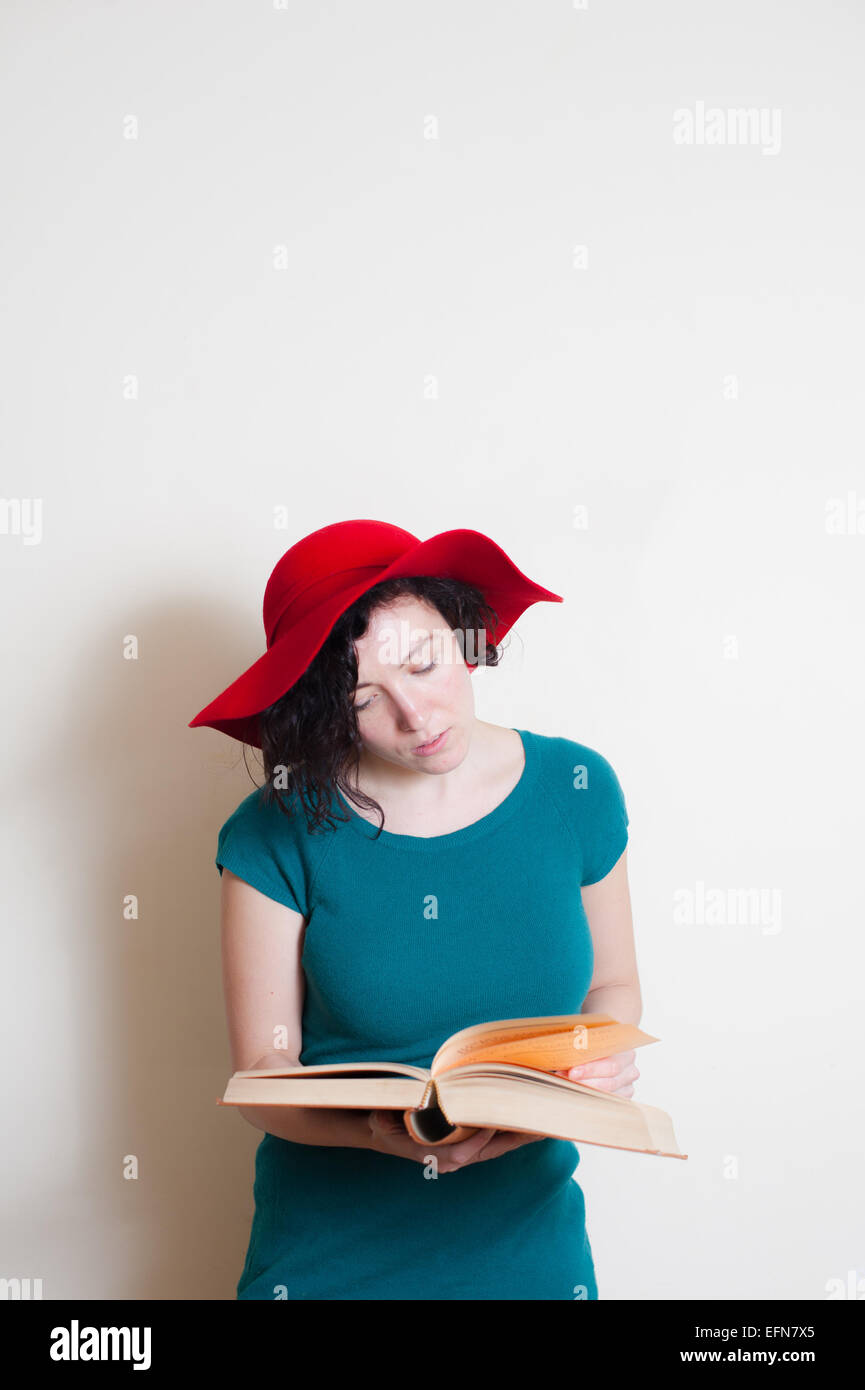 Jeune femme avec red hat lecture livre sur fond blanc Banque D'Images