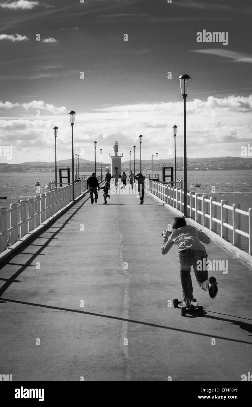 Photo en noir et blanc les uns flânant dans un quai et un enfant de la trottinette. Banque D'Images