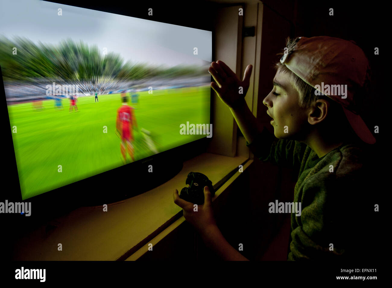 Un garçon avec une casquette de baseball à l'arrière joue un match de football avec sa console de jeux Banque D'Images