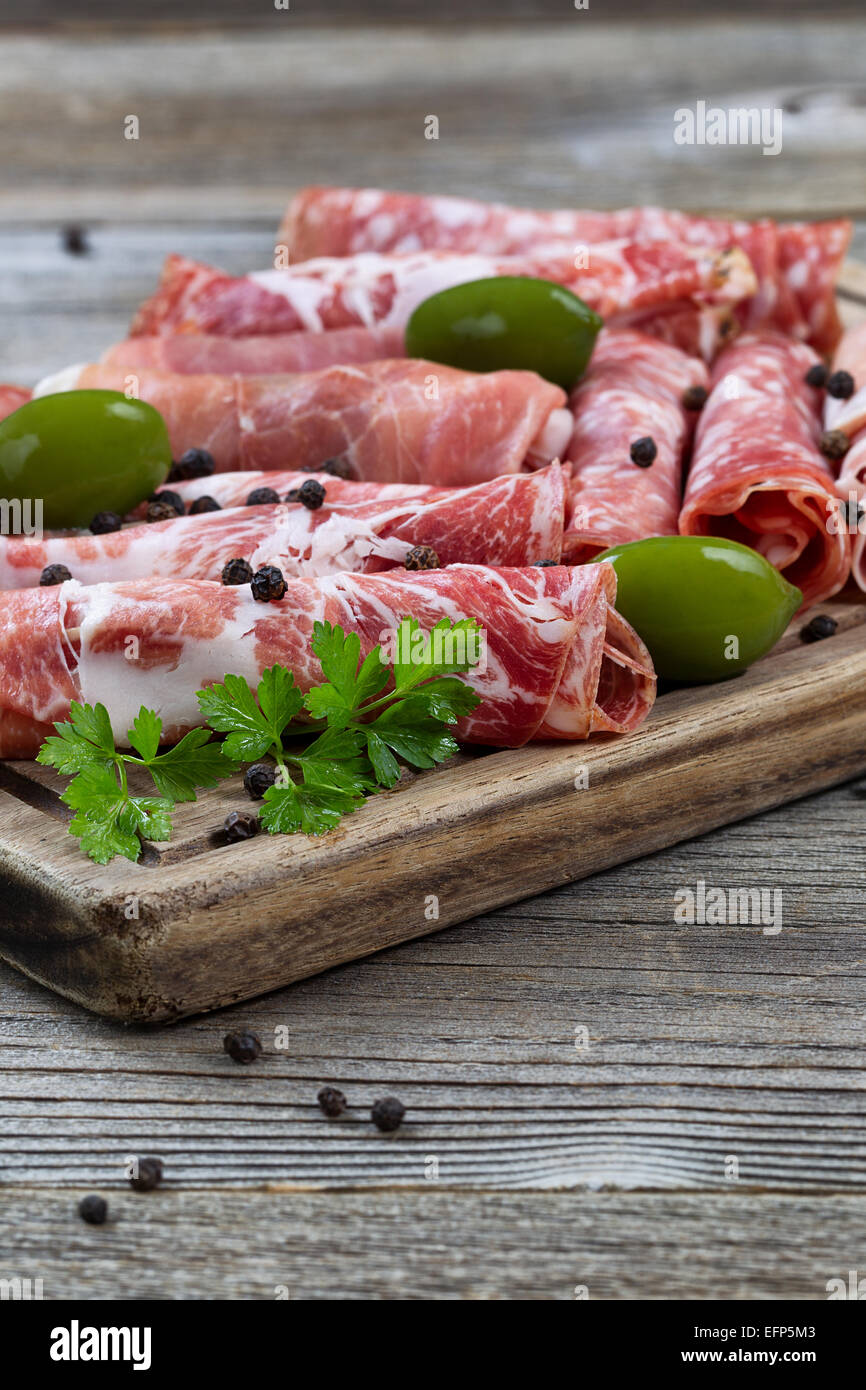 Close up vertical image de viandes diverses sur le service à bord avec du jambon, du porc, du boeuf, de persil et d'olives sur bois rustique. L'accent sur fro Banque D'Images