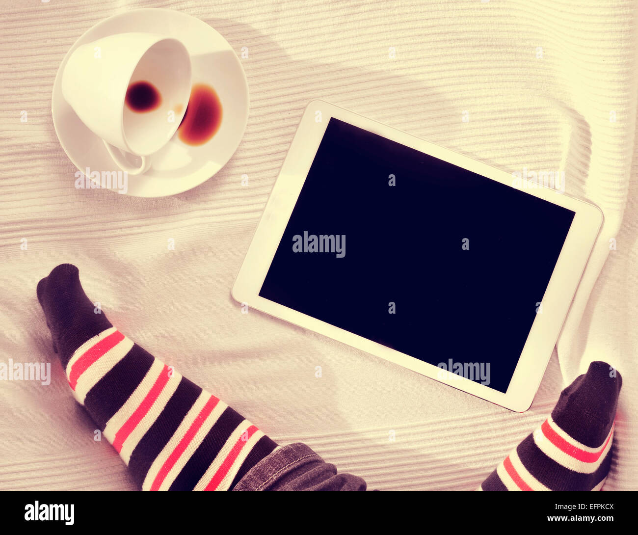 Un grand angle des pieds d'un homme et d'une tasse de café et un ordinateur tablette sur un lit recouvert d'un couvre-lit Banque D'Images Un grand angle des pieds d'un homme et d'une tasse de café et un ordinateur tablette sur un lit recouvert d'un couvre-lit Banque D'Images