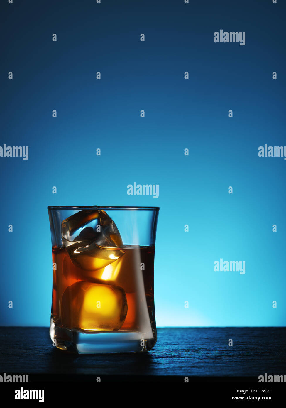 Verre de whisky avec de la glace sur un fond bleu. Banque D'Images