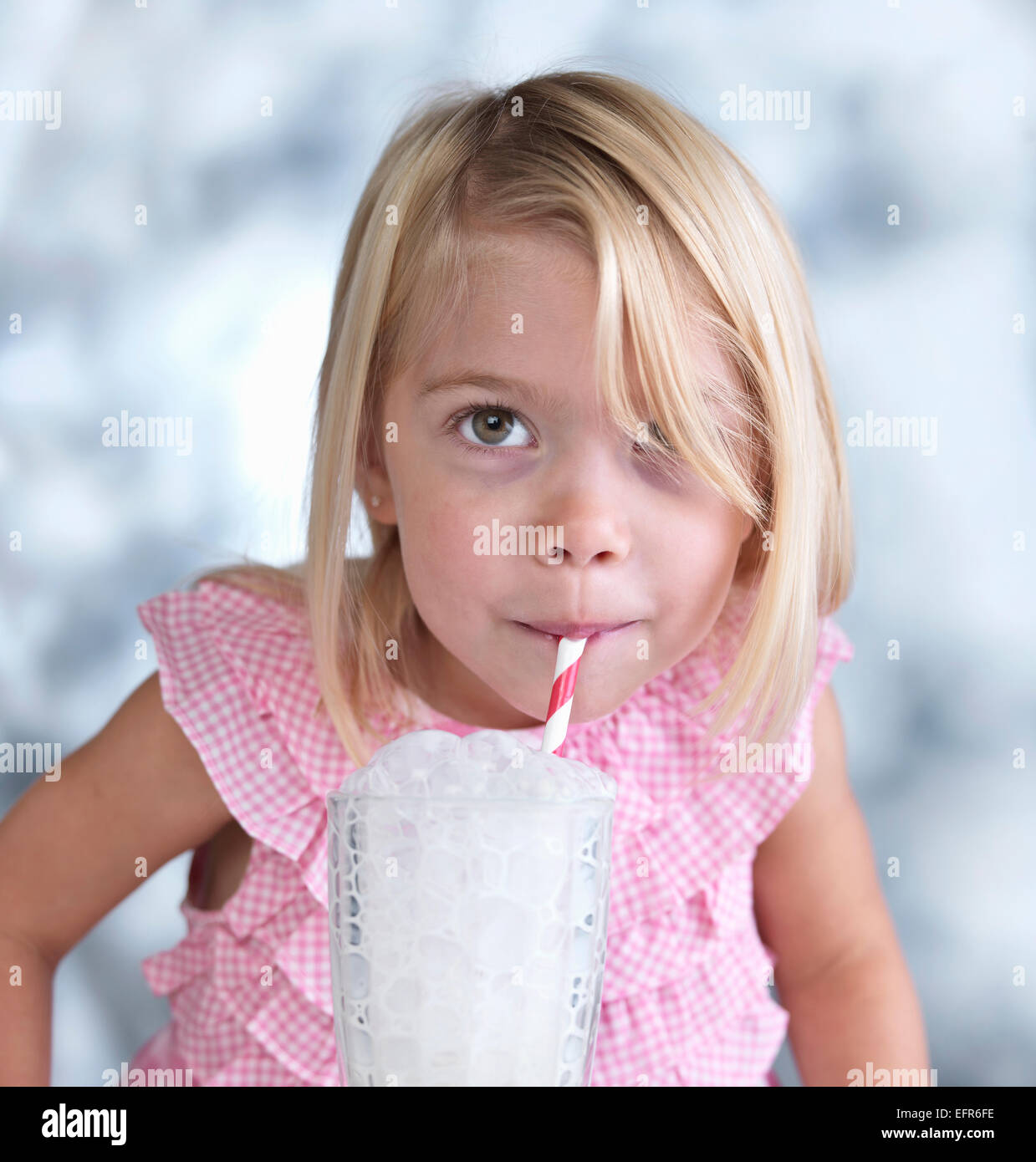 Portrait of cute female toddler faisant des bulles dans le verre de lait Banque D'Images