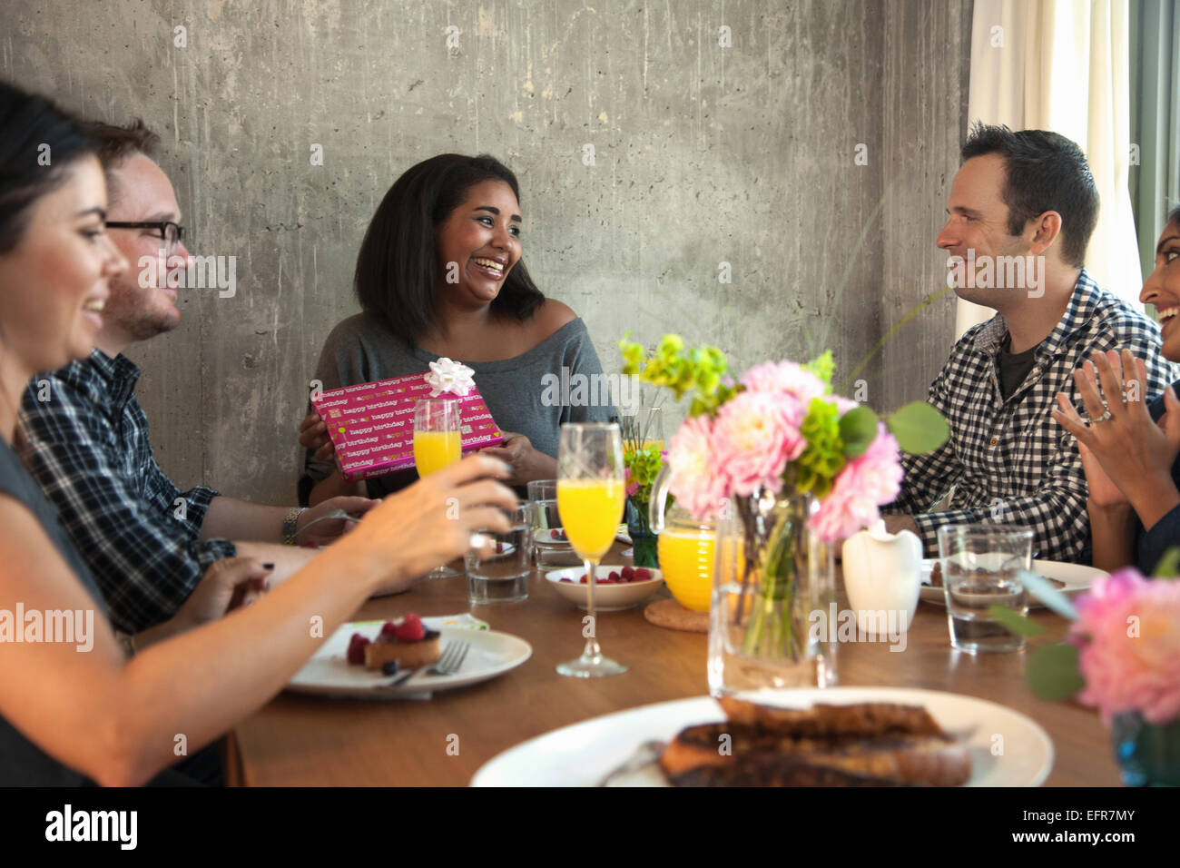 Groupe d'amis à la table de dîner, young woman holding wrapped gift Banque D'Images