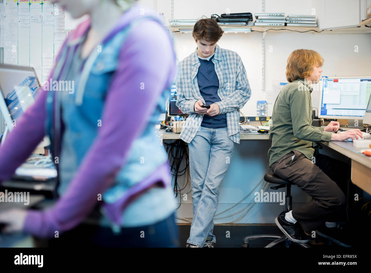 Trois personnes à un atelier de réparation d'ordinateur, un contrôle de son téléphone intelligent. Banque D'Images