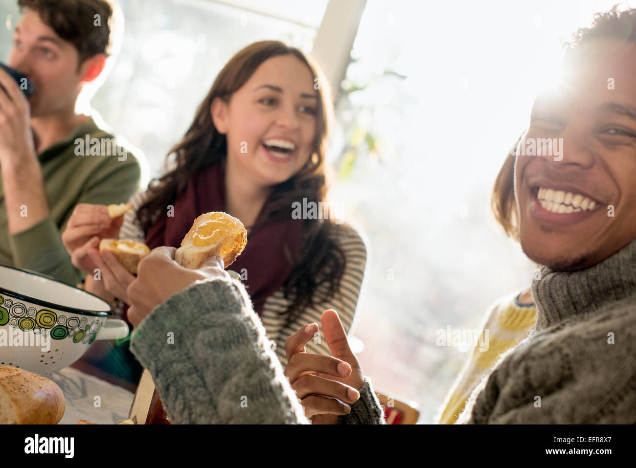 Trois personnes assises à une table, sourire, manger, boire et discuter. Banque D'Images