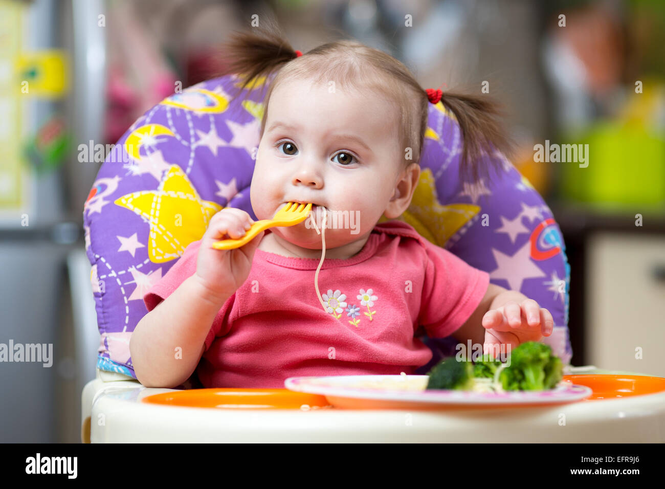 Bébé fille dans une chaise haute pour l'alimentation avec la fourchette et  la plaque Photo Stock - Alamy