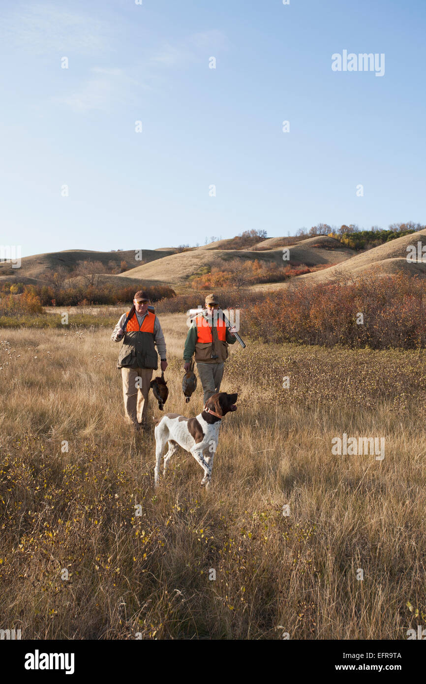 Deux hommes, les chasseurs d'oiseaux, avec des fusils, portant le sac du jour d'oiseaux morts, et d'un spaniel chien. Banque D'Images